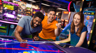 Three adults playing airhockey