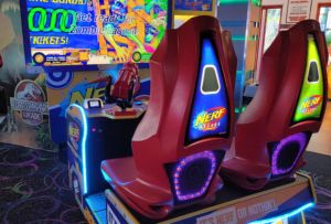 A brightly lit Nerf Arcade machine with two red seats, featuring colorful graphics and screens instructing players. Located near popular attractions like an indoor water park and laser tag in Coeur d'Alene, the game advertises a zombie lagoon and ticket bonuses.