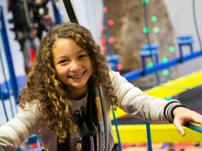 Young girl climbing through the ropes course smiling