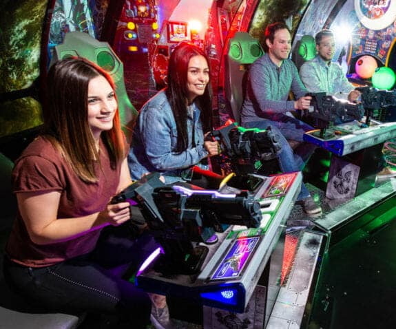 Group of young adults playing a group shooting game in the arcade