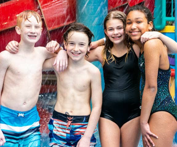 Two boys and two girls in swim suits standing in the water park smiling
