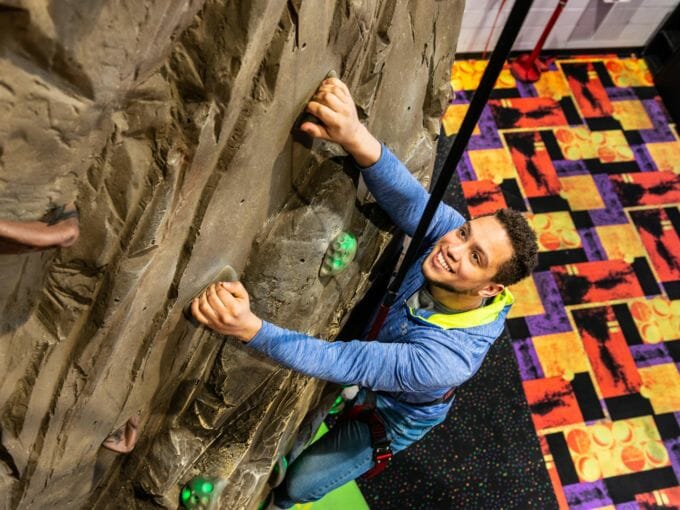 Young man climbing the rock wall in a harness