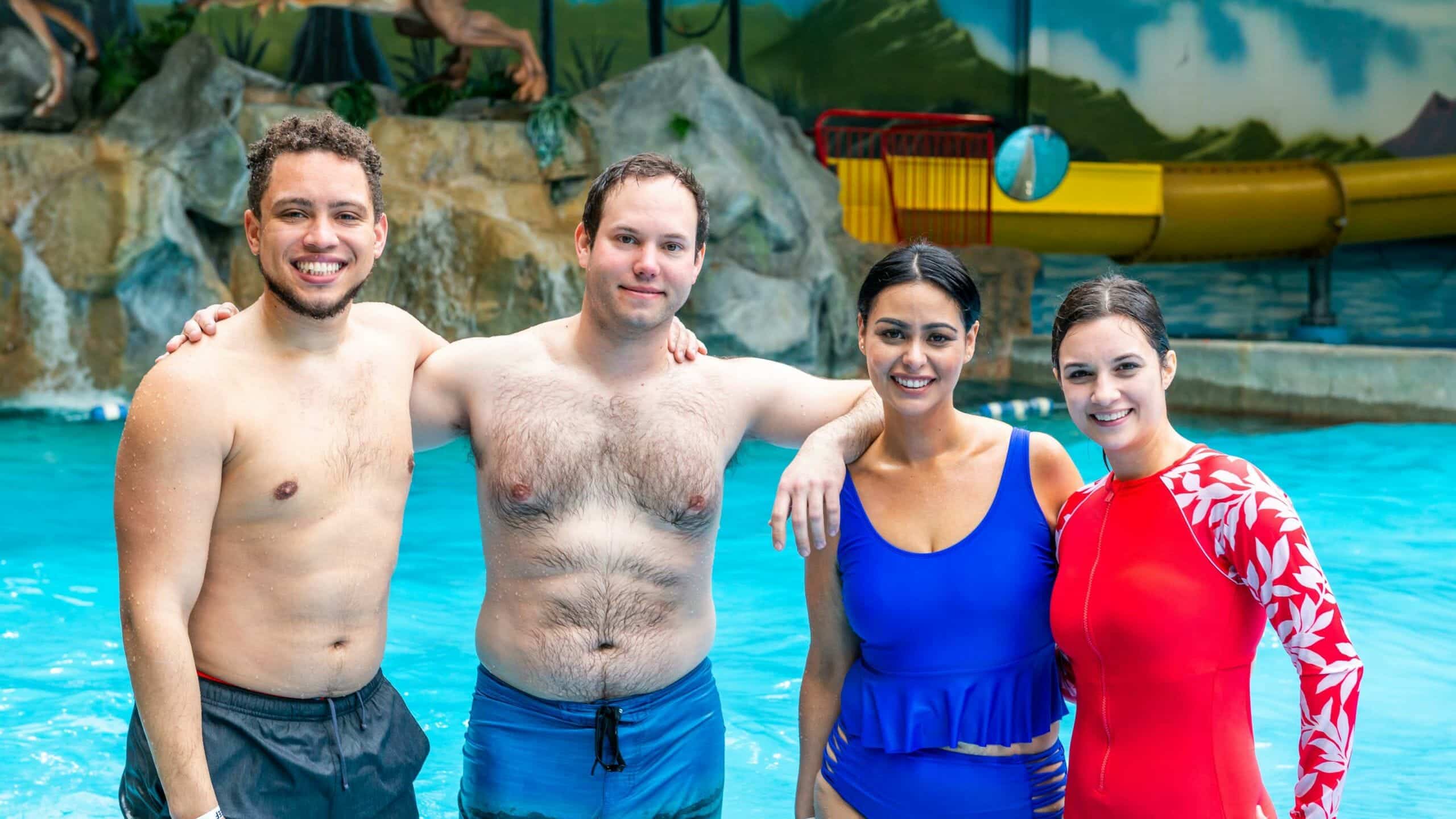 Four young adults in swim suits taking a group photo standing in the wave pool