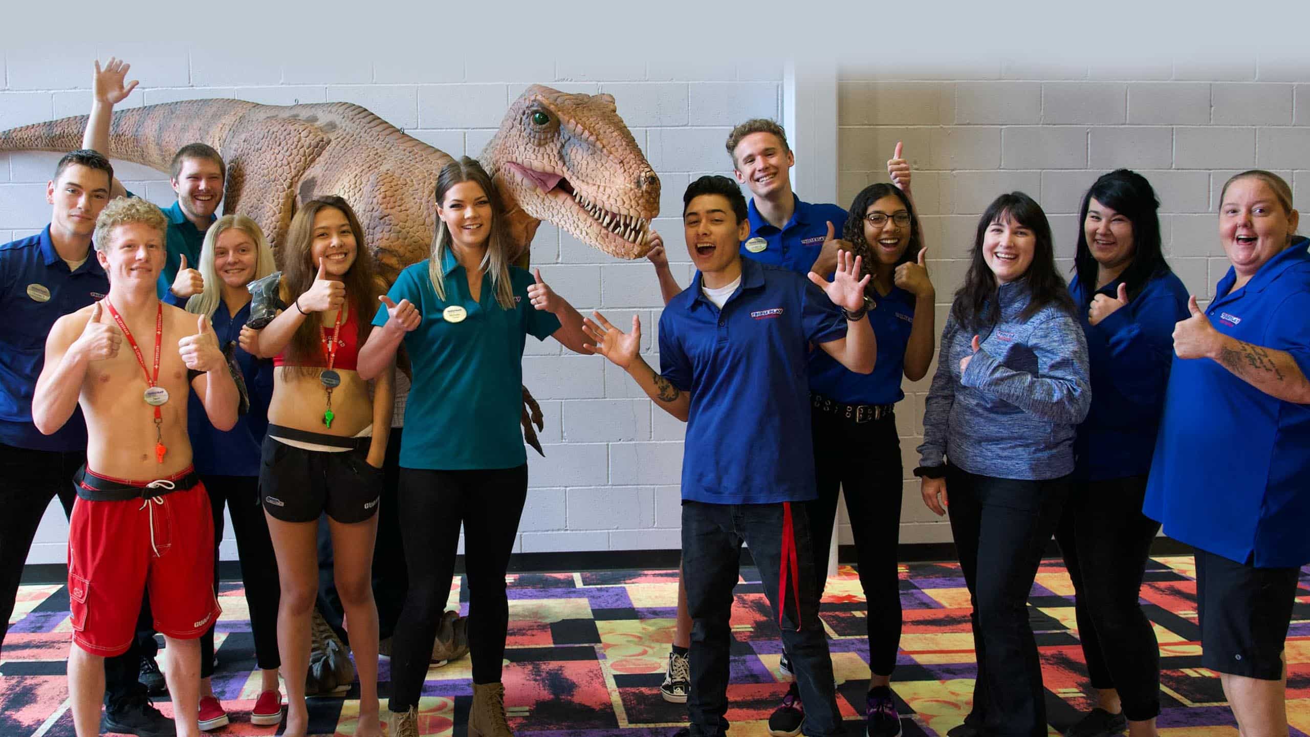 Group of Triple Play employees taking a group photo with thumbs up and Stanley the raptor behind them