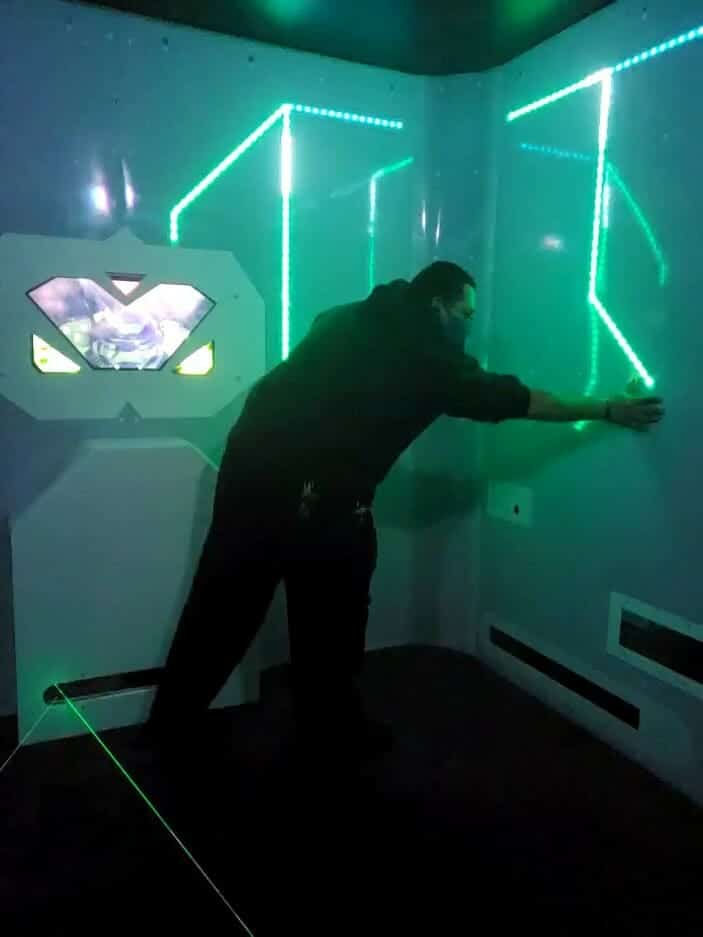 A person touches a wall with illuminated green lights in a dimly lit room with futuristic panels, reminiscent of the high-tech arenas found in a laser tag court d'Alene.